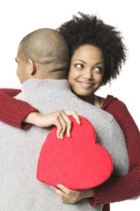 holiday portrait of a young adult woman as she holds a heart shaped box and hugs her boyfriend
